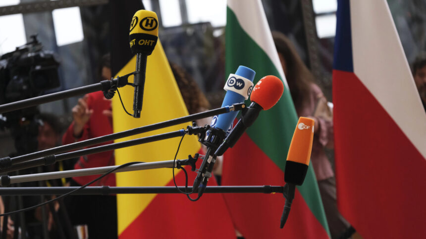 Television microphones in front of EU country flags.