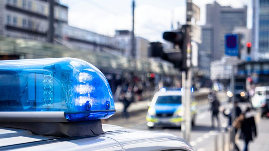 Straßenszene, im Vordergrund ein Blaulicht auf einem Polizeiauto, im Hintergrund unscharf Fußgänger:innen und ein weiteres Polizeiauto