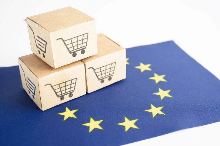 Drei Pappboxen mit Einkaufswagenzeichen auf einer EU-Flagge