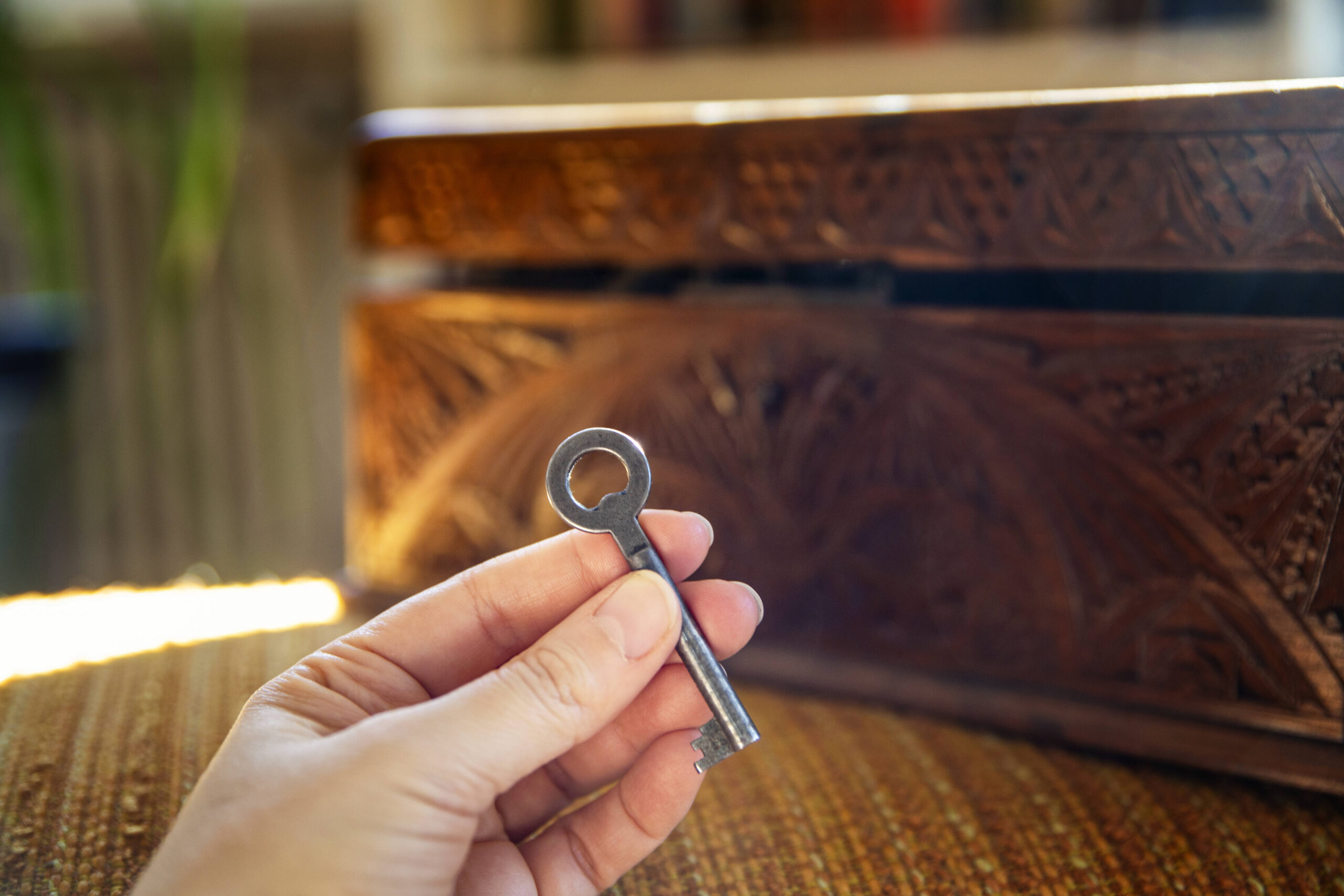 Eine Hand hält einen Schlüssel, im Hintergrund eine halb geöffnet Holzschatulle