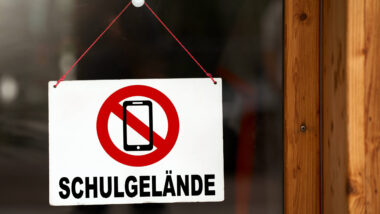 Schild an einer Glastür, darauf ein durchgestrichenes Handy, darunter steht "Schulgeände"