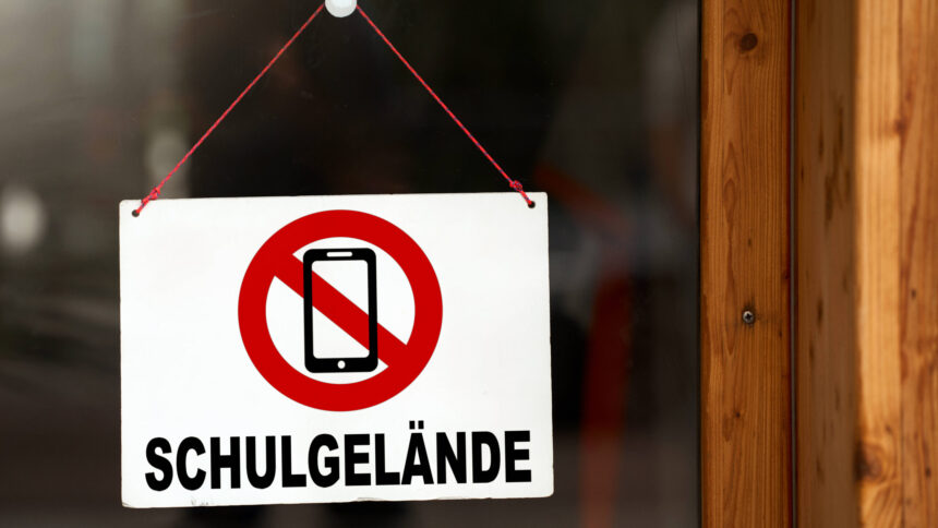 Schild an einer Glastür, darauf ein durchgestrichenes Handy, darunter steht "Schulgeände"