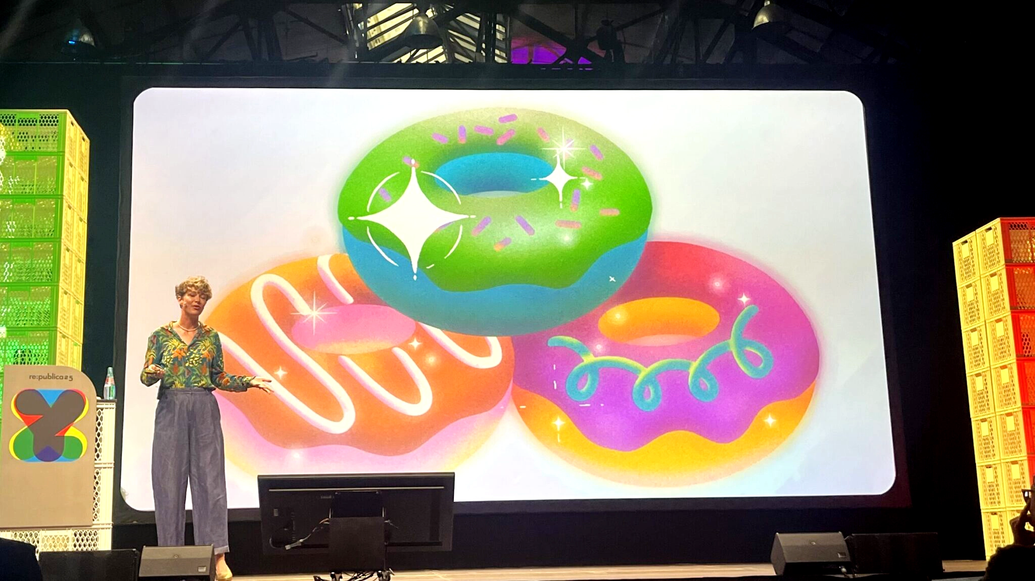Ein Mensch mit kurzen Haaren auf einer großen Bühne, auf dem riesigen Bildschirm im Hintergrund drei bunte Donuts