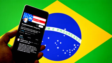 Eine brasilianische Flagge, davor ein Smartphone mit dem Social-Media-Posting von Donald Trump.