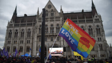 Menge mit Regenbogenfahne, vor einem historischen Gebäude