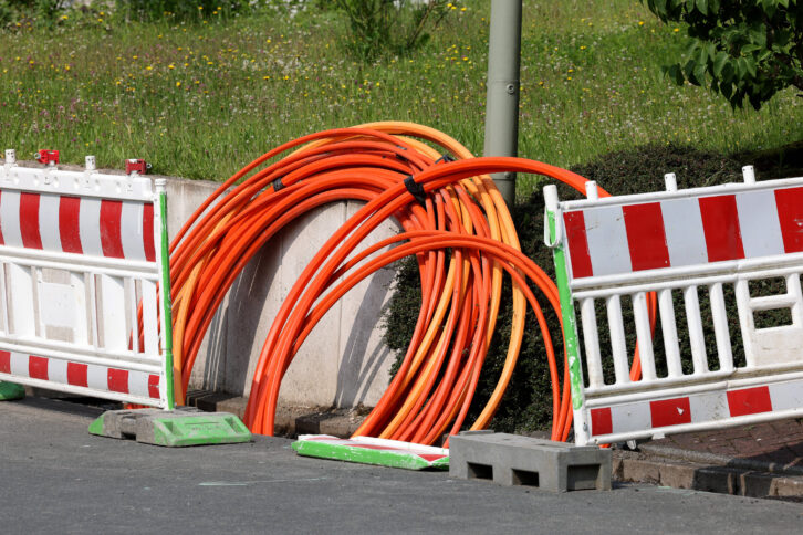 Glasfaserkabel in einem aufgebaggertem Loch mit Baustellenabsperrung.
