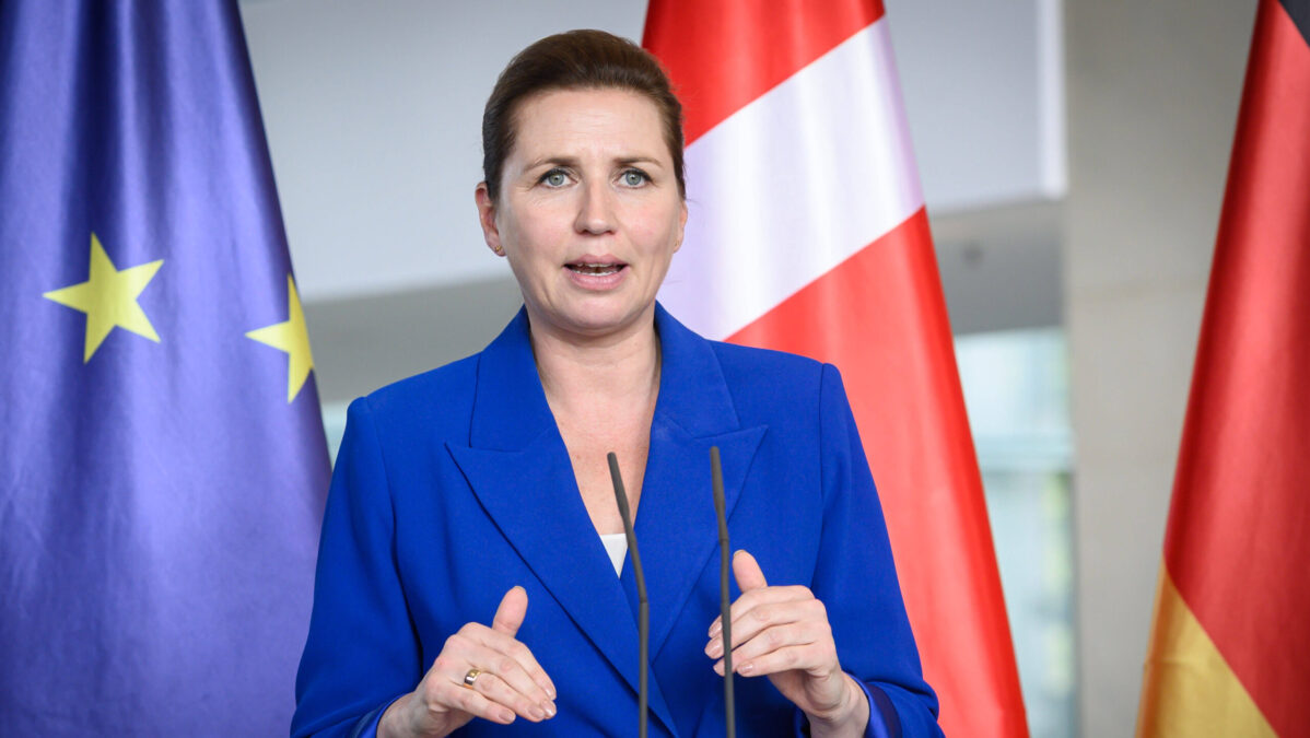 Mette Frederiksen steht während einer Pressekonferenz an einem Rednerpult vor der Fahne der EU, Dänemarks und Deutschlands.