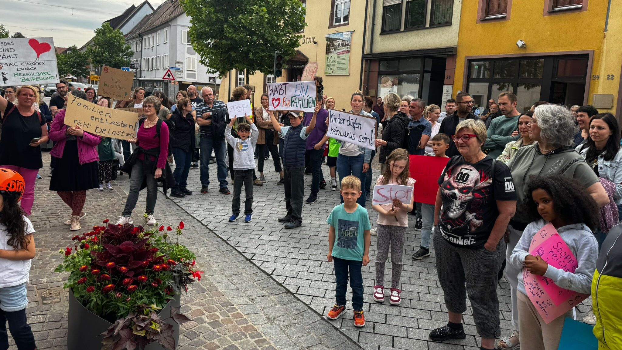Familien mit Schildern demonstrieren gegen hohe Kosten für Kindergarten.