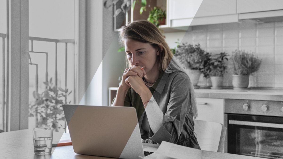 Eine Frau sitzt an einem Tisch und schaut ernst auf einen Laptop.
