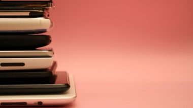 Ungefähr 10 gestapelte Smartphones vor rosa Hintergrund