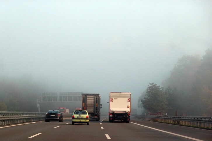 Blick auf eine Autobahn in Brandenburg, auf der ein paar Fahrzeuge in dichten Nebel fahren.
