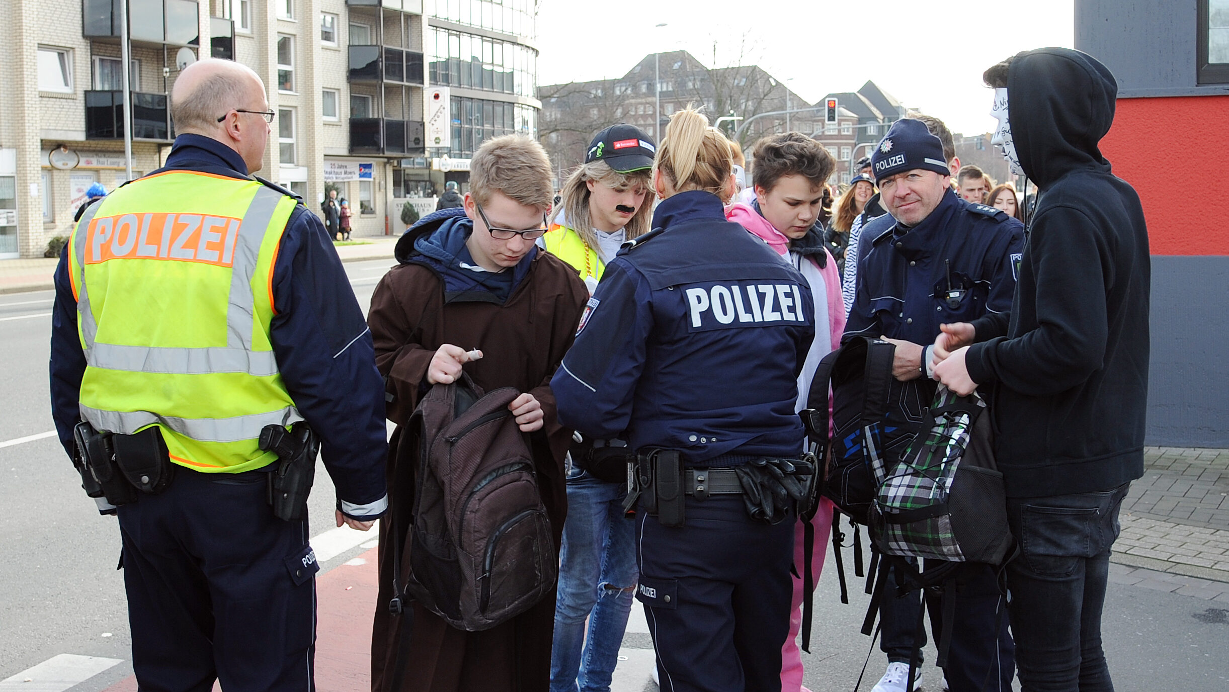 Polizisten durchsuchen Taschen von jungen Menschen.