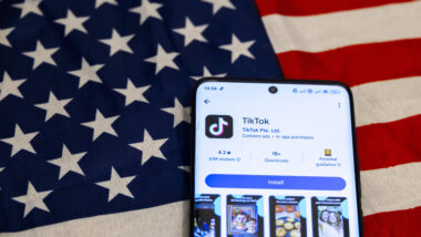 Smartphone liegt auf USA Fahne, TikTok wird im Appstore angezeigz
