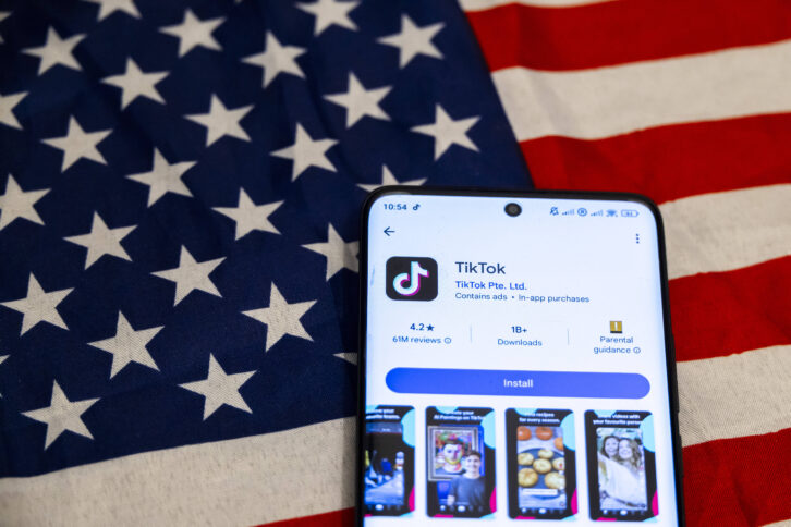 Smartphone liegt auf USA Fahne, TikTok wird im Appstore angezeigz