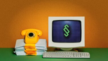Schreibtisch, auf dem ein Röhrenbildschirm mit einem Paragraf-Zeichen, davor eine Tastatur; daneben ein Stapel Papier, auf dem ein Telefon mit Wählscheibe steht