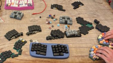 Selbstgebaute Tastaturen auf einem Holztisch, auf einer fertigen Tastatur tippen zwei Hände