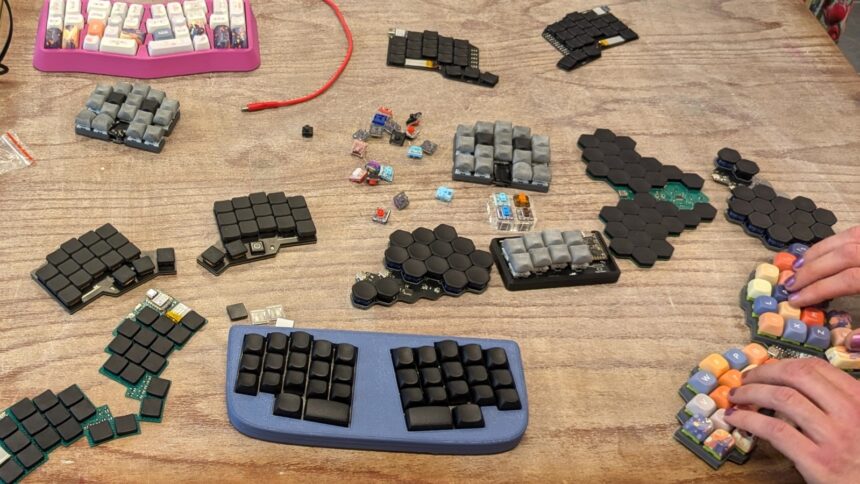 Selbstgebaute Tastaturen auf einem Holztisch, auf einer fertigen Tastatur tippen zwei Hände