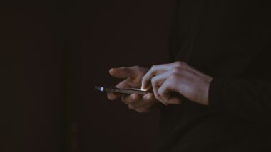 Düsteres Bild, nur zwei Hände sind beleuchtet, sie halten ein Smartphone