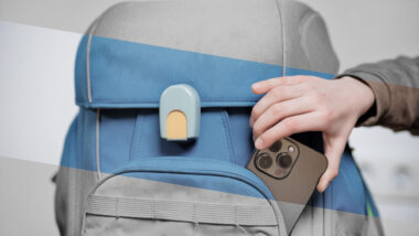 Eine Kinderhand steckt ein Smartphone in den Schulrucksack