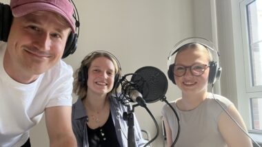 Drei Menschen mit großen Kopfhörern lächeln in die Kamera