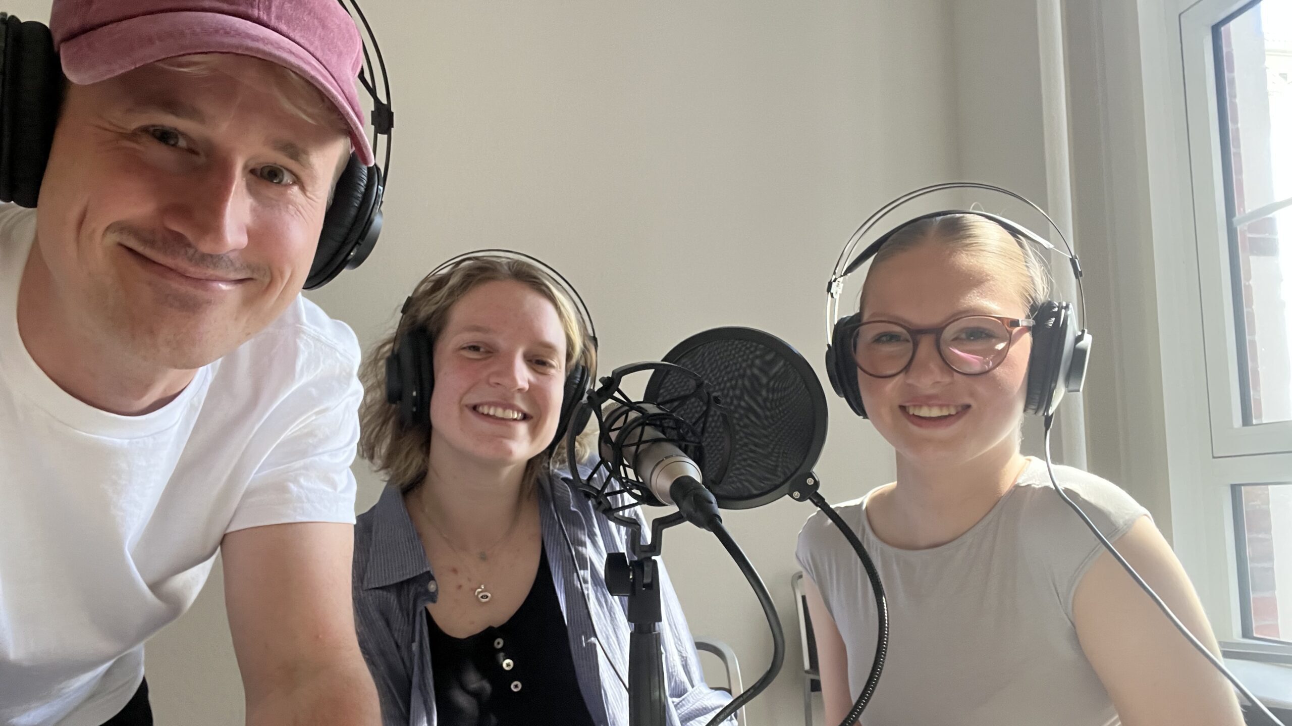 Drei Menschen mit großen Kopfhörern lächeln in die Kamera
