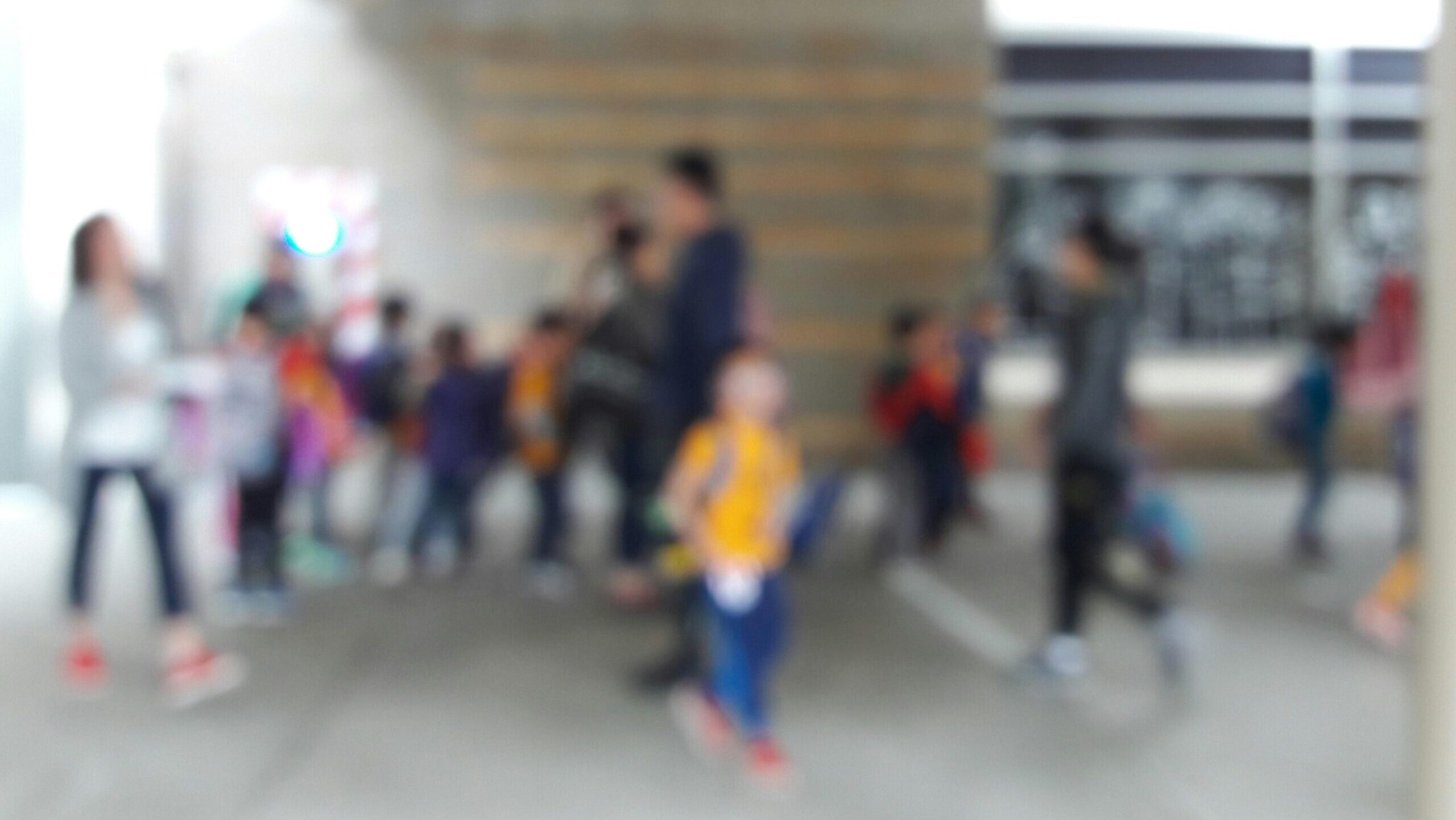 mehrere Kinder und Erwachsene laufen vor einem Schulgebäude her, sie sind nur verschwommen zu erkennen.