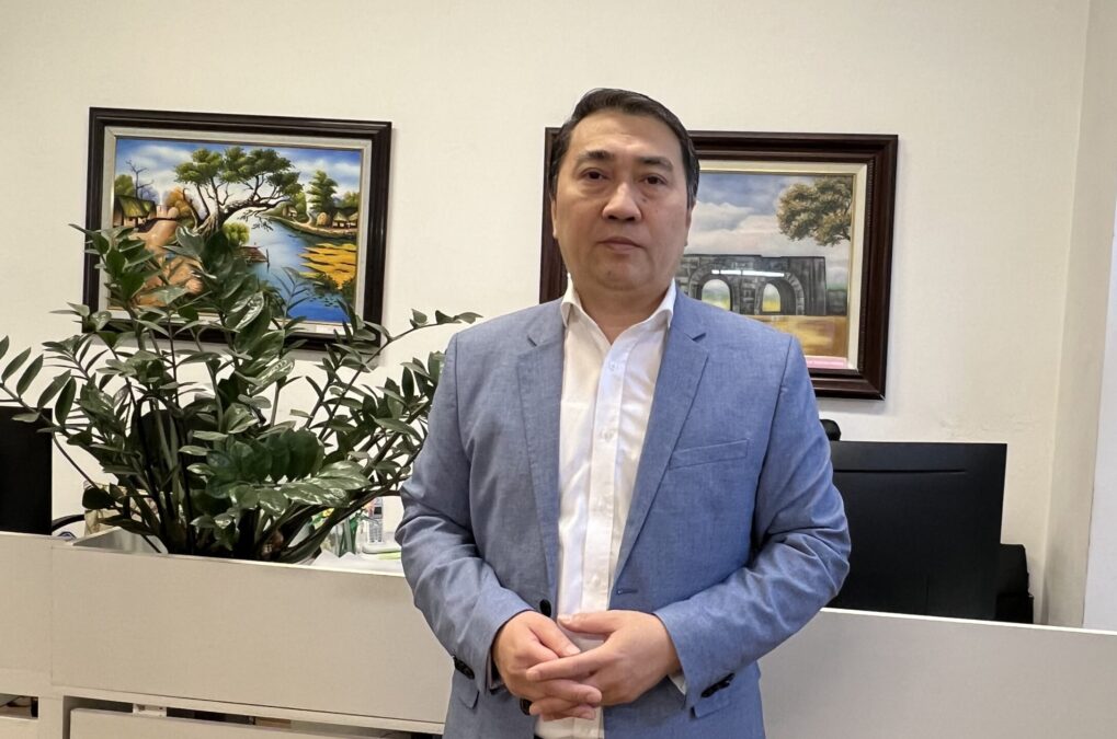 Der Journalist Trung Khoa Lê in einem Büro. Er hat ein weißes Hemd und eine blaue Anzugsjacke an.