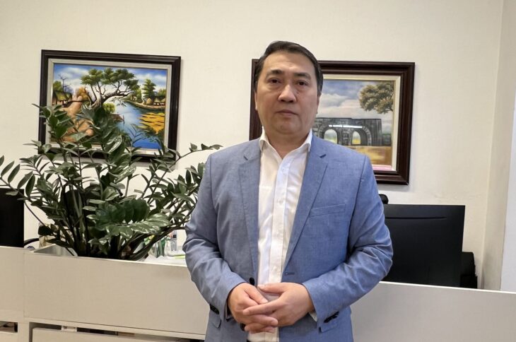 Der Journalist Trung Khoa Lê in einem Büro. Er hat ein weißes Hemd und eine blaue Anzugsjacke an.