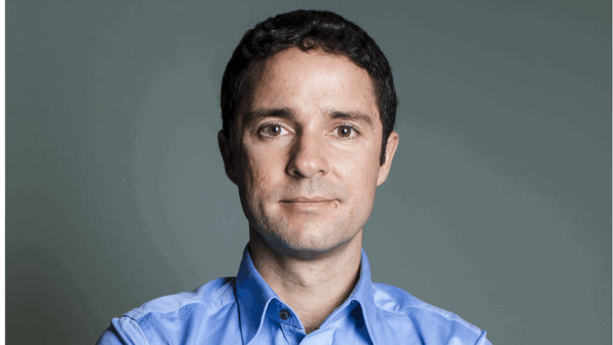 Eine Person in blauem Hemd und mit dunkel, kurzen Haaren schaut in die Kamera