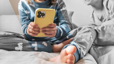 Zwei Kinder, eines hat ein gelbes Smartphone in der Hand. Die Gesichter sind nicht zu erkennen.