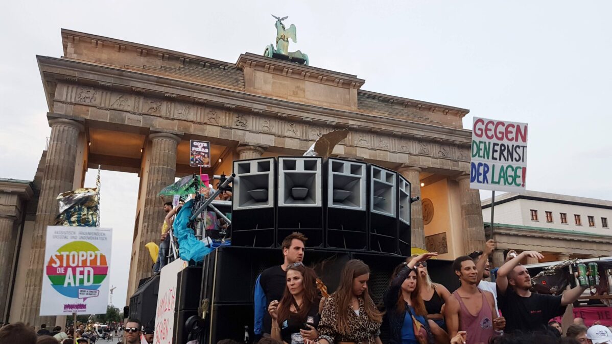 Menschen tanzen vor dem Brandenburger Tor während einer Demonstration gegen die AfD im Jahr 2018. Zu sehen sind große Lausprecherboxen.
