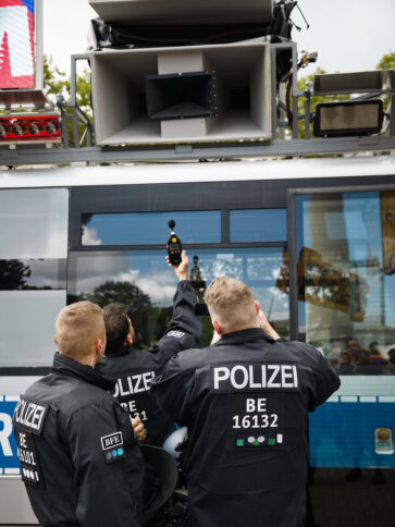 Drei Polizisten stehen mit einem Lautstärke-Messgerät vor einem Lautsprecher