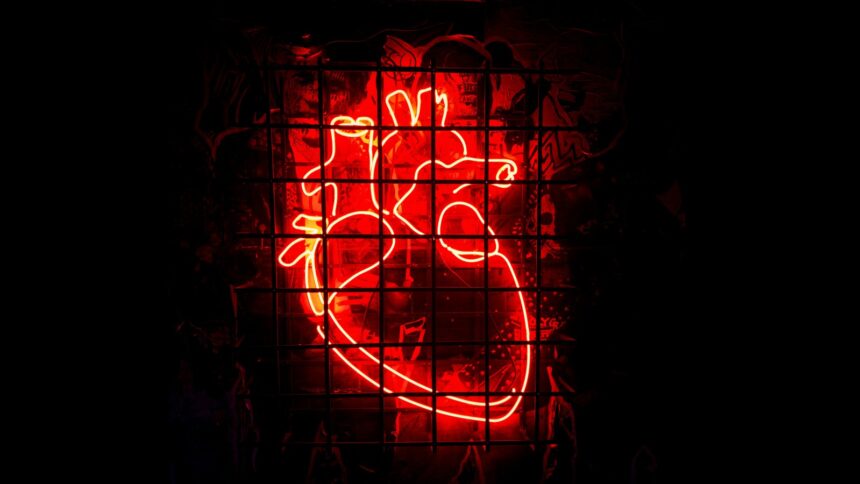 Ein rotleuchtendes Neonherz hinter einem Gitter vor dunklem Hintergrund