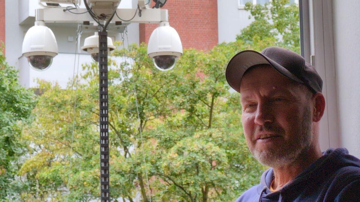 Ein Mann am Fenster, dahinter ein Kameraturm