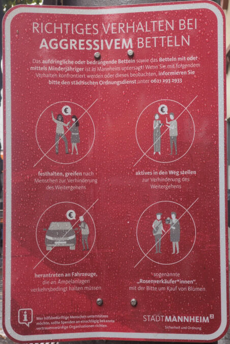 Ein rotes Schild, auf dem erklärt wird, angesichts welcher Arten von angeblich aggressivem Betteln Passant*innen das Ordnungsamt rufen sollen