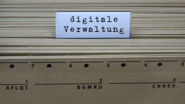 Auf Rücken von gelben Aktenordnern ist ein Trenner zu sehen. Auf ihm steht "digitale Verwaltung" geschrieben.