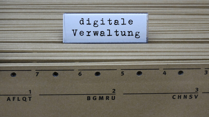 Auf Rücken von gelben Aktenordnern ist ein Trenner zu sehen. Auf ihm steht "digitale Verwaltung" geschrieben.