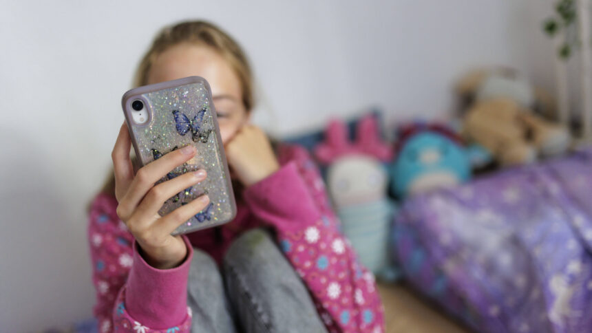 Mädchen schaut auf Handy, Gesicht von Handy verdeckt