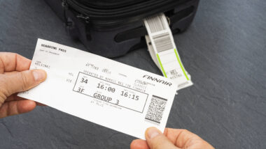 Zwei Hände halten eine Bordkarte von Finnair. Im Hintergrund ist ein schwarzer Koffer.