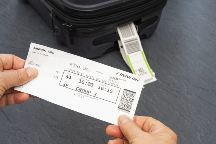Zwei Hände halten eine Bordkarte von Finnair. Im Hintergrund ist ein schwarzer Koffer.