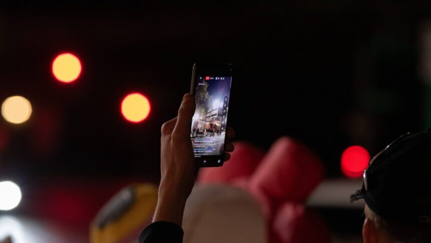 Smartphone wird in den Nachthimmel gehalten. Auf dem Bildschirm kann man den Livestream eines Protests erkennen.