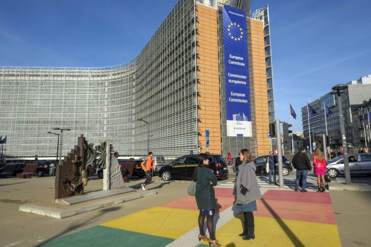 Bild des Gebäudes der EU-Kommission. Menschen stehen auf einem regenbogenfarbenden Fußgängerüberweg vor dem Gebäude.