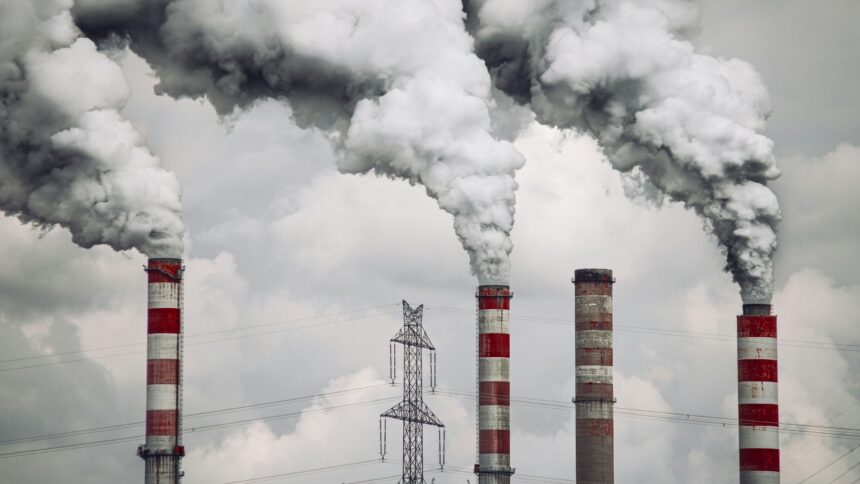 Schornsteine vor bewölktem Himmel aus denen Rauchwolken quillen