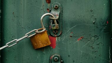 Ein offenes Schloss mit einer Metalkette an einer rostigen Halterung.