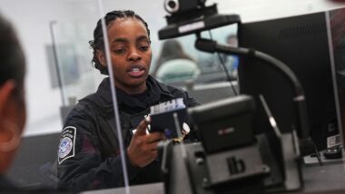 Eine Beamtin der US-Grenzschutzbehörde fertigt einen Reisenden am Washington International Thurgood Marshall Airport ab. Im Vordergrund ein Gerät mit Kamera.