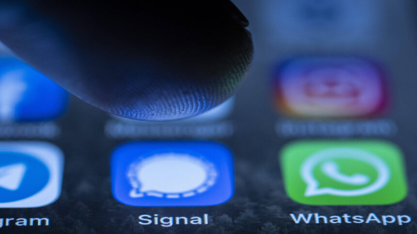 Smartphone-Bildschirm mit den Logos von Signal und WhatsApp und einem Finger, der draufdrücken will.