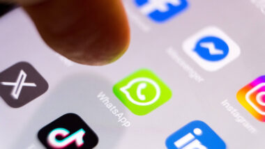 Auf einem Smartphone Bildschirm sind Apps zu sehen. Ein Finger schwebt über dem WhatsApp-Symbol.