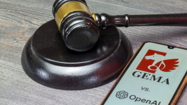 Ein Richterhammer und ein Smartphone liegen auf einer Holzoberfläche. Das Smartphone zeigt das Logo der Gema und von OpenAI, dazwischen steht ein "versus".