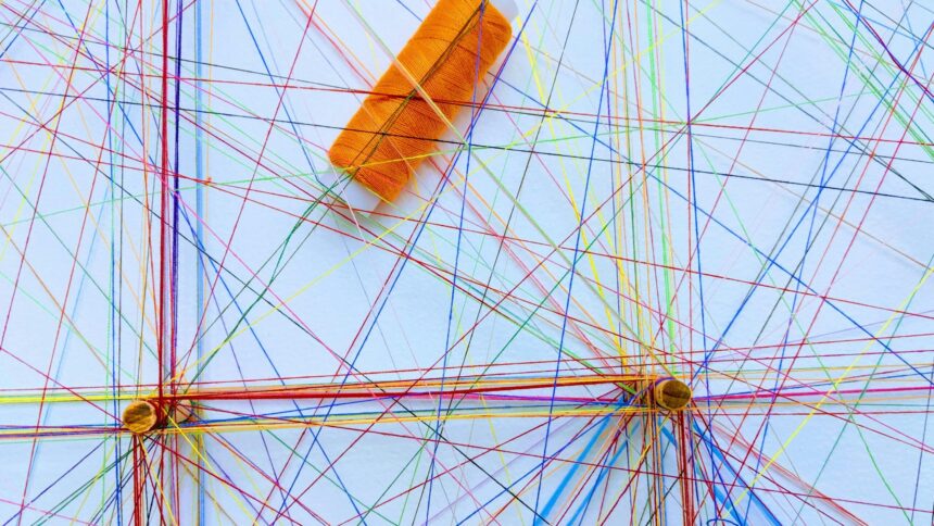 bunte Nähfäden, die über einer hellen Fläche kreuz und quer gespannt sind