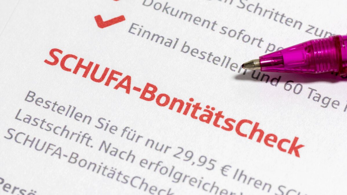 Ein Pinker Kugelschreiber zeigt auf auf einen großen, roten Schriftzug der sich "SCHUFA-BonitätsCheck" ließt.
